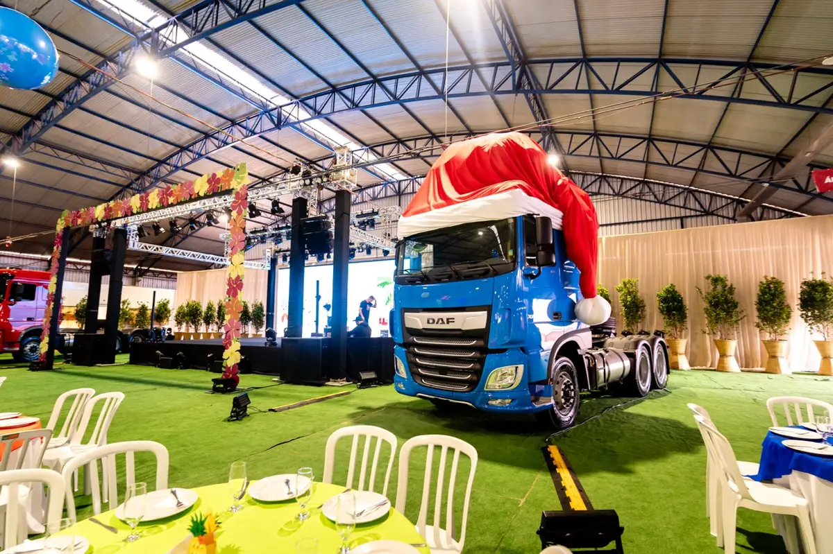 Caminhão azul com um grande chapéu de Papai Noel vermelho em grande evento corporativo decorado com mesas e cadeiras